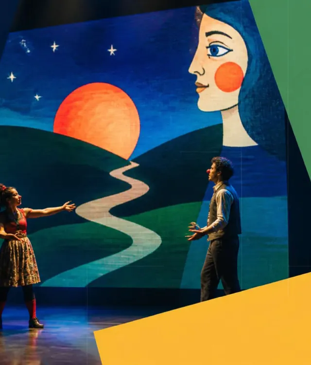 Cena em palco: casal diante de um painel de LED com paisagem animada ao pôr do sol