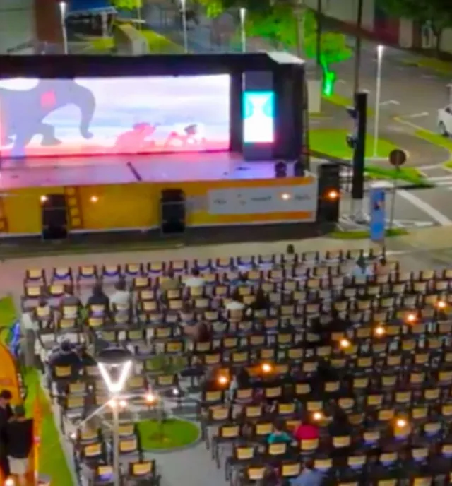 Vista aérea de uma praça à noite com painel de LED e cadeiras para o público
