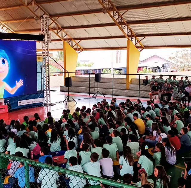 Quadra escolar coberta com painel de LED e estudantes assistindo